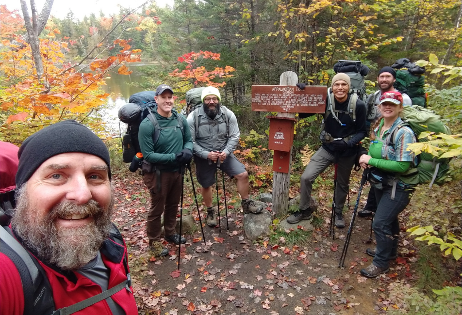 five men and one woman posing for a photo while hiking